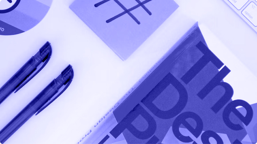 Overhead view of two pens beside a sticky note marked with a grid and an open magazine set in oversized display type.